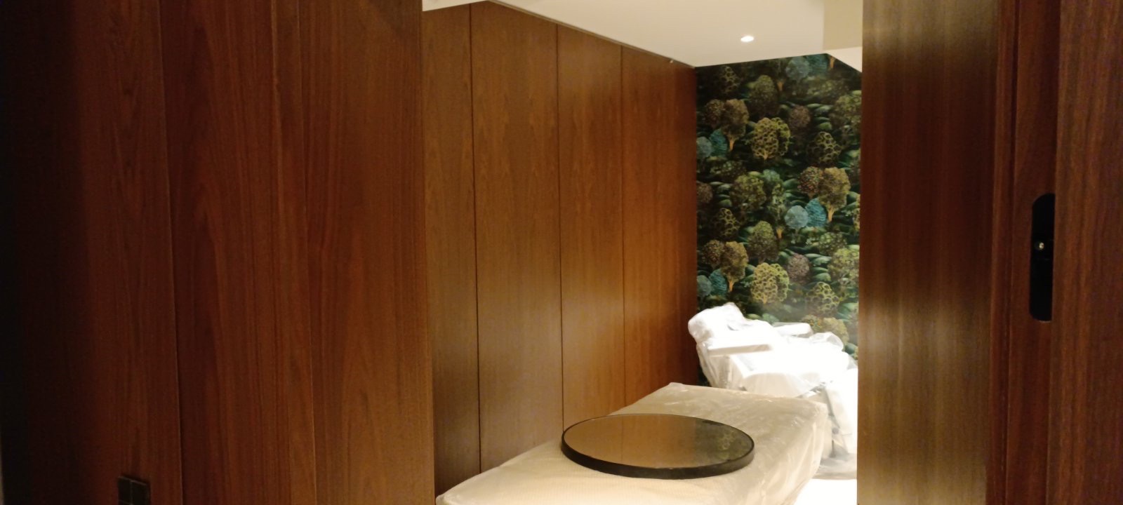 Room with wooden panel walls, floral mural, covered chairs, and a round table resting on a covered surface.